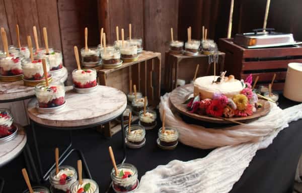 A photo of a dessert display at a wedding with a wedding cake and Mason Jar Desserts