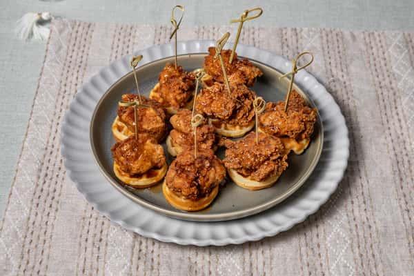 Mini chicken and waffle skewers drizzled with maple glaze, served on a scalloped metal plate—perfect for brunch buffets, soul food-inspired catering, or comfort food events.
