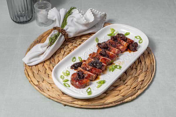 Glazed pork tenderloin medallions topped with fig compote and garnished with green onions, served on an elegant white platter with a woven charger—perfect for refined Southern dining or holiday catering.