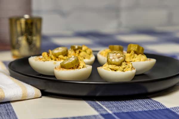 Southern-style deviled eggs garnished with sliced pickled okra and paprika, arranged on a matte black plate—perfect for classic comfort food menus or party platters.