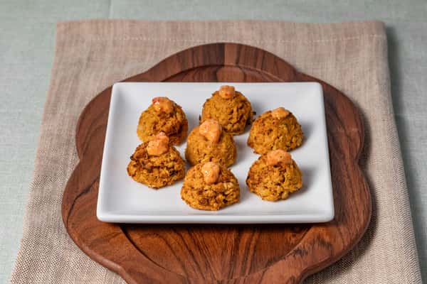 Mini crab cakes or hush puppies topped with a dollop of spicy remoulade, served on a square white plate over a wooden cutting board—ideal for seafood starters or Southern-inspired catering.