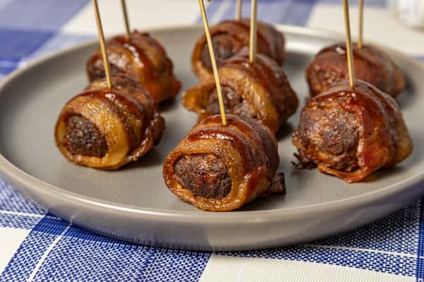 Bacon-wrapped meatballs served on a gray ceramic plate with toothpicks, ideal as a savory appetizer or party snack, showcased on a blue and white checkered tablecloth.