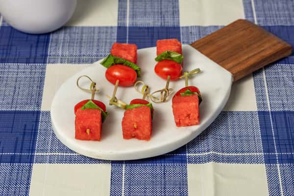 Refreshing watermelon, cherry tomato, and basil skewers served on a white marble board—perfect for summer appetizers or vegan finger food menus.