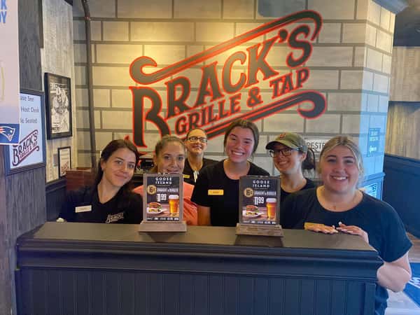 Friendly Brack's Grille & Tap team members gathered at the host stand beneath the restaurant's signature logo, welcoming guests with warm hospitality.