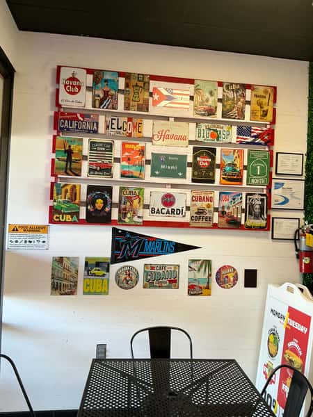 The interior of a Cuban restaurant features the counter, equipment, and seating area. The wall décor displays a variety of license plates and signs with Cuban and Miami themes.