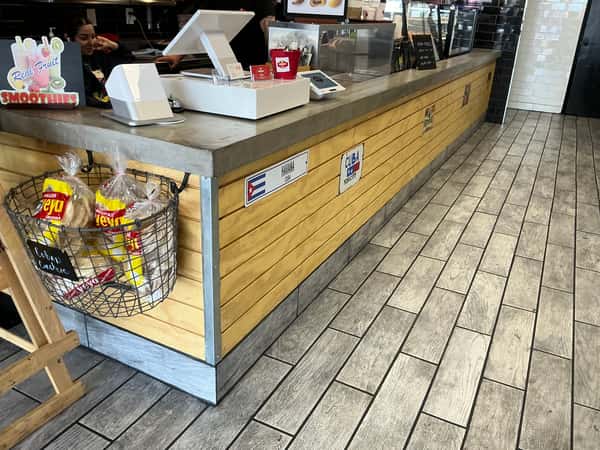 The service counter at Havana Express has a concrete countertop, and a wooden base with metal trim and Havana Cuba signage. A basket of bread and pastries hangs from the side. Text: "Real Fruit SMOOTHIES", "Cuban Bread".