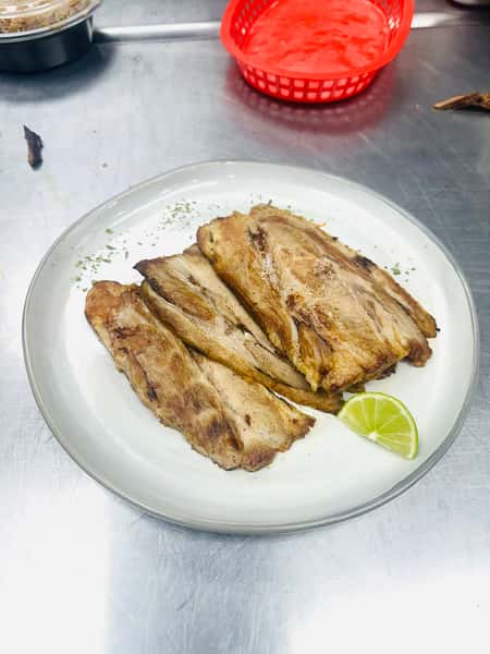 Cuban cuisine shines in this photo of grilled pork, served sliced on a gray plate. It's garnished with a lime wedge and a sprinkle of herbs.