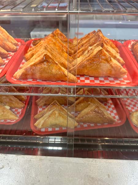 Freshly baked Cuban pastries are displayed in a glass case, ready to be enjoyed from the Havana Express Cuban Restaurant & Bakery. The golden pastries sit on red and white checkered paper.