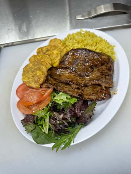 Cuban cuisine shines in this image of a grilled steak dish. Accompanying the steak are sides of yellow rice, plantains, a fresh salad, and tomato slices.