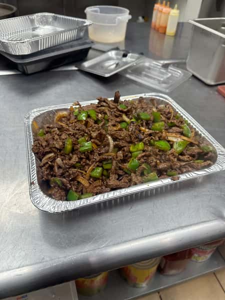 Cuban cuisine shines in this photo of grilled beef, with onions and peppers, served on a foil tray. It could be part of a catering service.