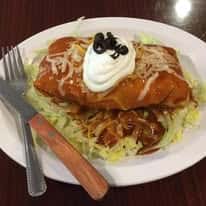 Smothered burrito topped with shredded cheese, sour cream, and black olives, served on a bed of shredded lettuce.