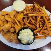 Plate of fried chicken, potato wedges, and French fries served with coleslaw and a side of dipping sauce.
