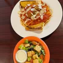 Plate of spaghetti with meatballs, marinara sauce, shaved parmesan, and garlic bread, served with a side salad and ranch dressing.