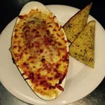 Baked cheesy pasta dish served in an oval bowl with two pieces of garlic bread on a white plate.