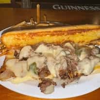 Philly cheesesteak sandwich loaded with melted cheese, sautéed onions, and green peppers, served with a side of fries.