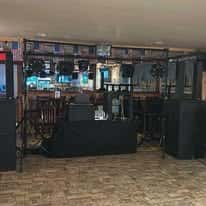 DJ booth setup with speakers and lighting equipment in a bar area, with American flag decor and wooden flooring.