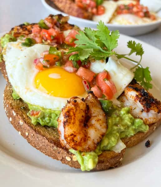 Avocado toast with fried egg, grilled shrimp, tomato salsa, and cilantro on toast.