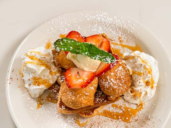 French toast nuggets with sliced strawberries, whipped cream, a mint sprig, powdered sugar, and syrup.
