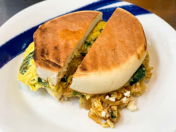 Breakfast sandwich of egg, spinach, caramelized onions, and feta on a toasted English muffin, cut in half.