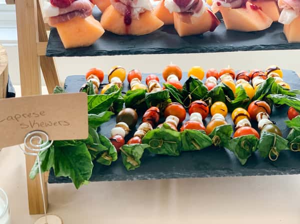 Caprese skewers with cherry tomatoes, mozzarella balls, basil, and balsamic glaze on a slate tray.