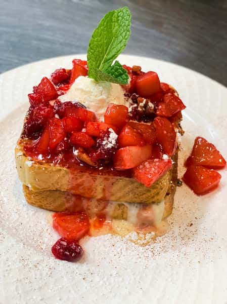 French toast topped with glazed strawberries, a dollop of cream, and a mint leaf, dusted with powdered sugar.