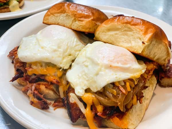 Breakfast sliders with fried eggs, melted cheese, onions, and meat on small buns.