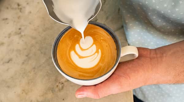 Barista pouring steamed milk into espresso to create fresh latte art.