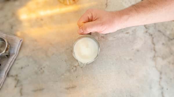 Cafe Remedy | Hand holding a glass pitcher filled with white liquid on a light-colored countertop.