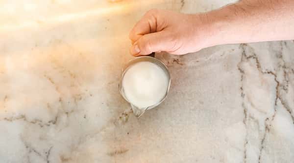Overhead view of freshly steamed milk in a small pitcher on a marble countertop.