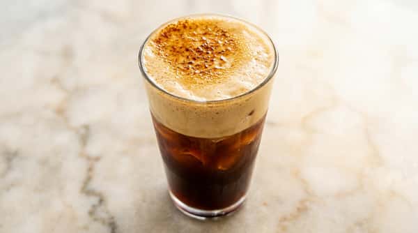 Iced coffee topped with creamy foam and a caramelized finish on a marble countertop.