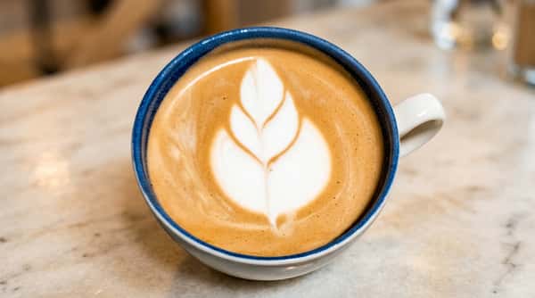 Cafe Remedy | Latte in a white and blue ceramic mug with a delicate white foamed leaf design on top.