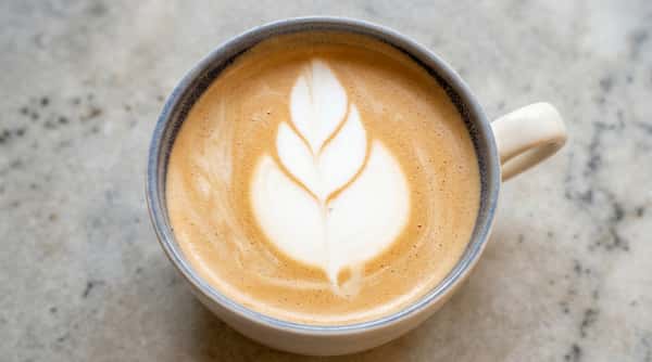 Fresh latte topped with leaf-shaped foam art in a white ceramic cup.