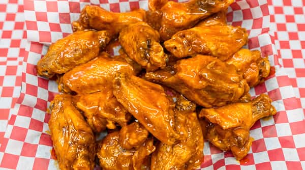 Pile of chicken wings coated in a shiny orange sauce, served in a basket lined with red and white checkered paper.