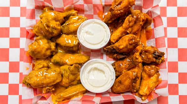Two portions of chicken wings, some coated in orange sauce, others in reddish-orange sauce, served with white dipping sauces in paper baskets.