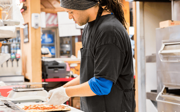 Employee prepping a pizza for the oven