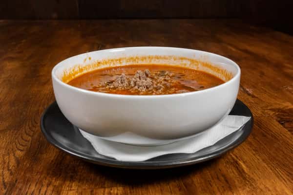 Side view of a bowl of rustic Italian sausage soup with tomato broth, spinach, and crumbled sausage, served with a napkin-lined black plate.