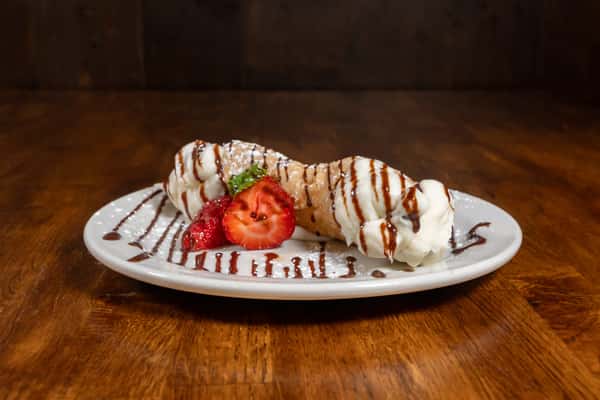 Classic Italian cannoli filled with sweet ricotta cream, drizzled with chocolate syrup and garnished with fresh strawberries and mint on a white dessert plate.