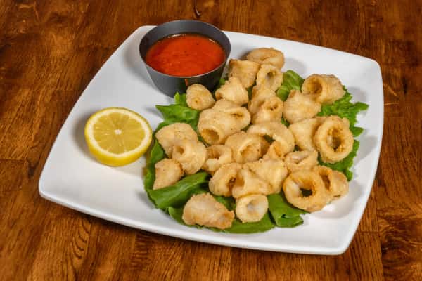 Fried calamari rings on a bed of lettuce, accompanied by a lemon wedge and marinara dipping sauce.