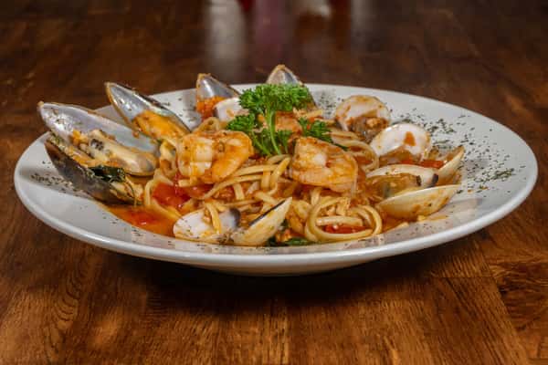 Seafood pasta with linguine, shrimp, clams, and mussels in a garlic tomato sauce, garnished with parsley and served on a white plate.