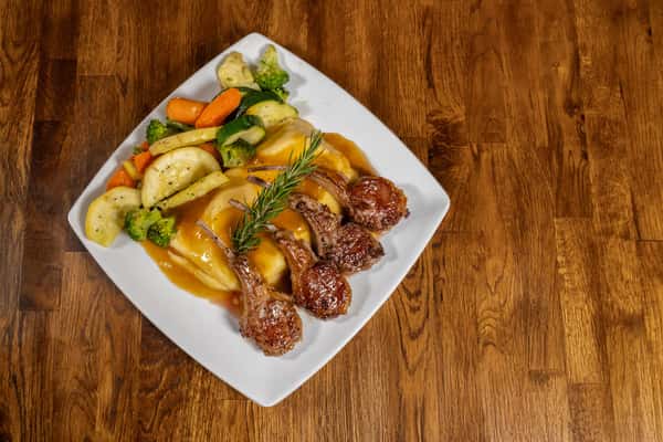 Grilled lamb chops served over mashed potatoes with brown gravy, accompanied by sautéed mixed vegetables and garnished with rosemary.