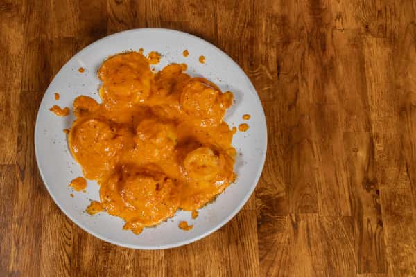 Pillowy cheese ravioli smothered in a rich tomato cream sauce, served on a white plate over a rustic wooden table.