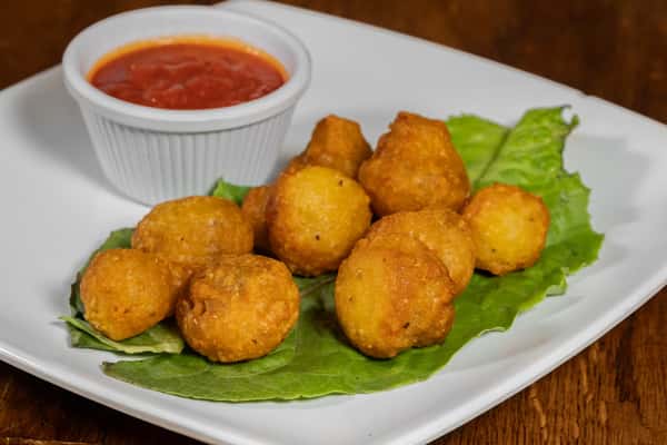 Golden fried cheese balls served on a bed of lettuce with a side of marinara dipping sauce on a square white plate.