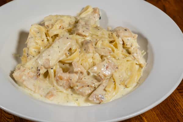 Creamy chicken Alfredo fettuccine with grilled chicken pieces tossed in a rich garlic‑cream sauce, served in a white bowl.