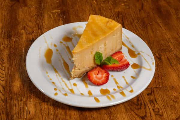 Slice of creamy caramel cheesecake garnished with strawberries and mint, with caramel sauce drizzled around the plate.