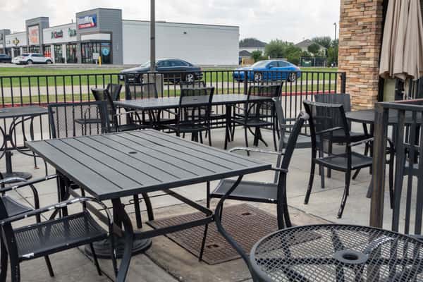 Restaurant outdoor patio seating with black metal tables and chairs overlooking a street and nearby shops.