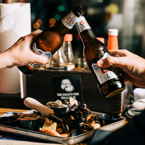 Friends cheerfully clink beer bottles together over a seafood platter