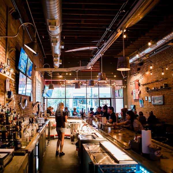 Interior view of a bustling bar area at Shuckin' Shack, featuring patrons enjoying seafood at a bright, inviting establishment.