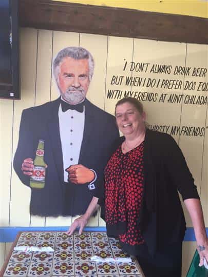 a customer smiling and posing next to the painting of the most interesting man in the world