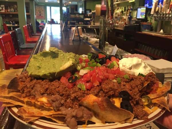 a plate of nachos with beef, pico de gallo, guacamole, sour cream, olives, and cheese on top