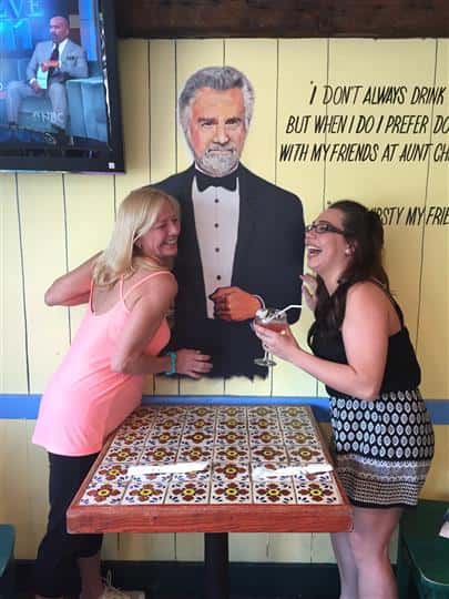 Two customers laughing with a painting of the most interesting man in the world